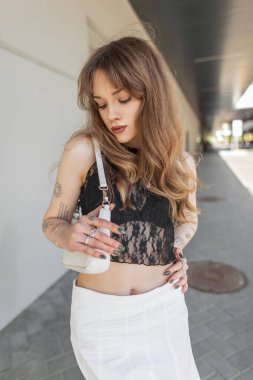 Moda dantelli siyah bluzlu, beyaz çantalı sütyenli, kollarında dövmesi olan şık, hippi bir erkek manken.