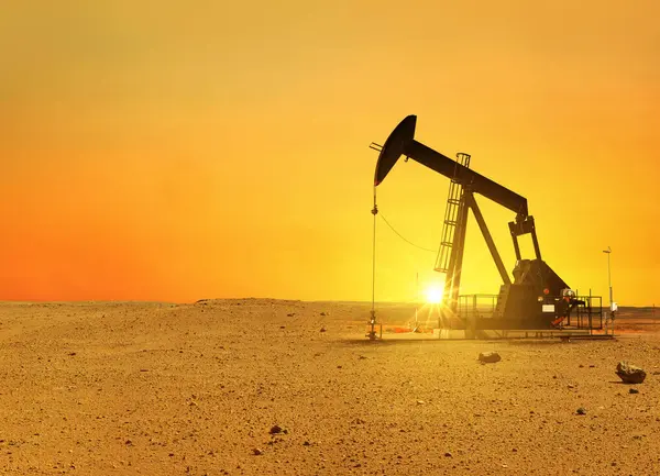 Pumpjack rig pumps oil in the desert at sunset. Dead land and sand, concept. Global warming, creative idea. Resources Energy of planet Earth.