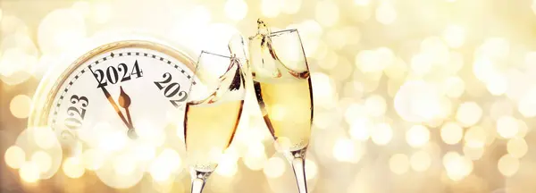 Vintage gold clock strikes New Year 2024 with glasses of champagne on a beige background with bokeh lights. New Year 2024 and Christmas card, creative idea. Start of the party and celebration holiday