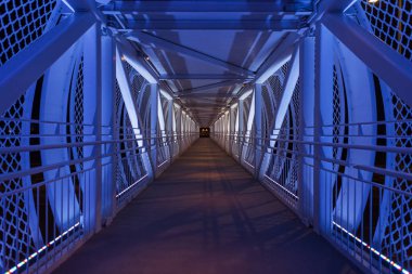 Geceleri mavi ışıkları olan güzel bir ayak köprüsü. Köprü boyunca uzanan yol. Geçiş