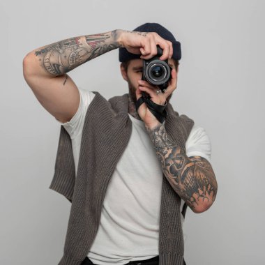 Moda örgü kazaklı şapkalı yakışıklı yaratıcı hippi stüdyoda aynasız fotoğraf makinesi ile fotoğraf çekiyor.