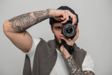 Örgü şapkalı ve kazaklı yakışıklı hippi fotoğrafçı stüdyoda fotoğraf çekiyor ve kameraya bakıyor..