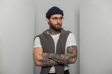 Havalı, sakallı, bıyıklı, dövmeli, şık gözlüklü, moda beyaz tişörtlü, süveterli bir şapka giyen yakışıklı hippi.