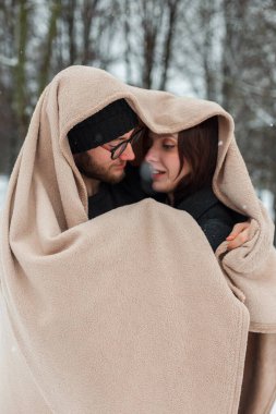 Bir kış günü parkta bej bir battaniyeye sarılı mutlu bir çift sevgili.