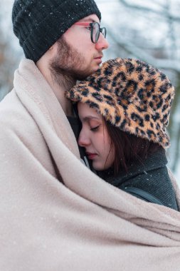 Şehvetli, genç aşıklar sıcak bej bir battaniyeye sarılıp kış parkında kar altında duruyorlar. Duygular, sevgi ve sarılmalar. Sevgililer Günün kutlu olsun.