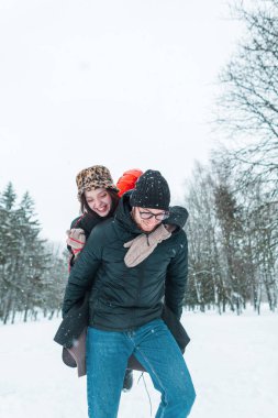 Parkta kız arkadaşını sırtında taşıyan mutlu yakışıklı genç adam. Güzel, neşeli aşıklar kış günü karla birlikte eğleniyorlar.