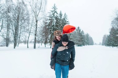 Güzel, mutlu aşıklar kış parkında kar yağarken eğleniyorlar. Sevgililer gününde sırtında kız taşıyan yakışıklı bir adam.