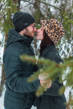 Güzel moda aşıkları, şık kış kıyafetleri içinde karlı bir günde ormanda sarılıp öpüşürler.