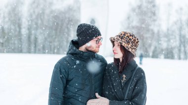 Moda kıyafetleri içinde genç ve güzel aşıklar kış parkında karlı bir şekilde birlikte yürürler. Yakışıklı bir adam ve şık bir kız.