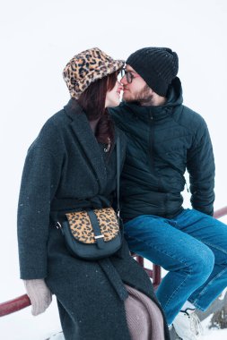 Kış kıyafetleri içinde bir kış parkında oturup öpüşen güzel, genç aşıklar.