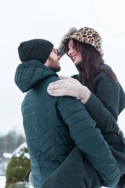 Şapkalı, örgü eldivenli ve ceketli şık kış kıyafetleri içinde mutlu ve genç aşıklar dışarıda eğleniyorlar. Adam güzel bir kızı kollarında tutuyor gülümseyerek