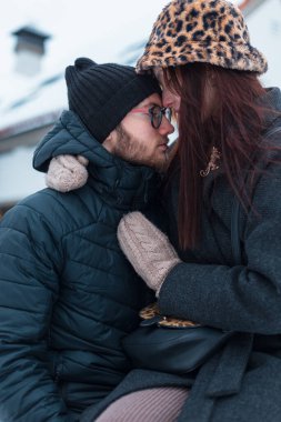Güzel sokak aşıkları, şık kışlık giysiler içinde, ceketli ve eldivenli şapkalı bir çift şehirde oturuyor ve sarılıyorlar.