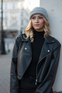 Şehirde şık, şık, sarışın, siyah, sıradan, deri ceketli ve süveterli bir şapka takan bir kız. Sevimli kadın.