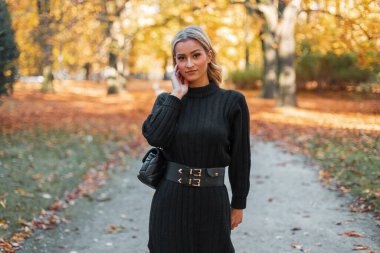 Güz parkında sarı yapraklı çantalı, siyah örülü güzel bir sonbahar kızı yürüyor.