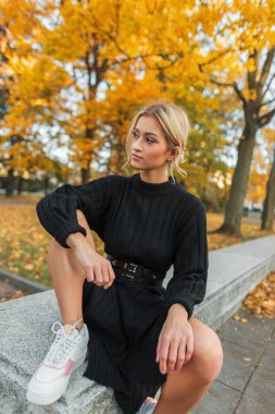 Güz parkında sarı yapraklı beyaz spor ayakkabılarla siyah örülü güzel bir kadın mankeni.