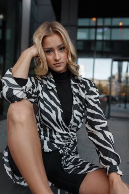 Şık zebra desenli elbisesi ve beyaz spor ayakkabılı şortu olan güzel bir kız şehirde oturur ve dinlenir.