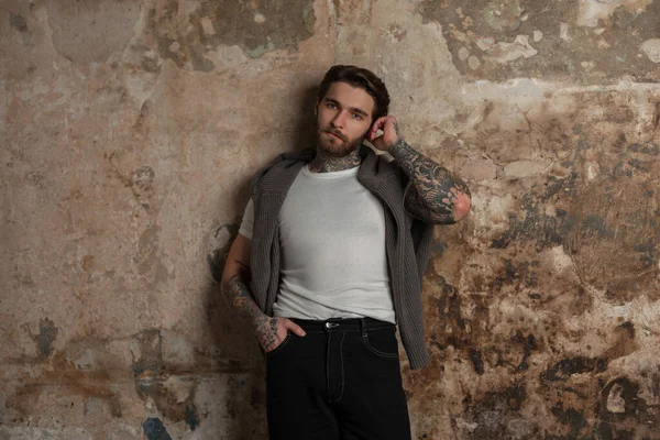 Havalı, şık, genç, hippi bir model. Moda kıyafetler, örgü süveter ve beyaz tişört, eski bir grunge duvarının yanında duruyor.