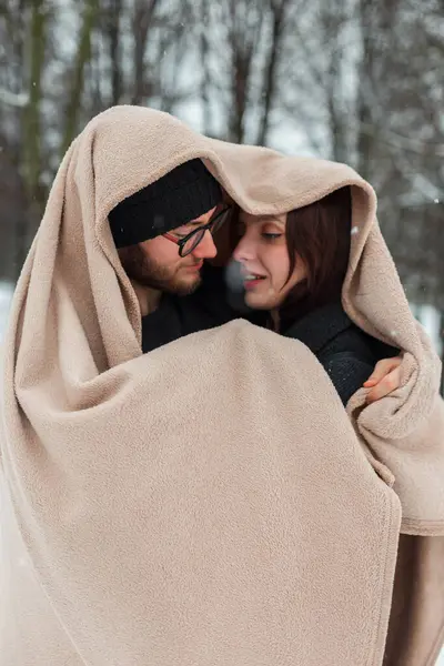 Bir kış günü parkta bej bir battaniyeye sarılı mutlu bir çift sevgili.