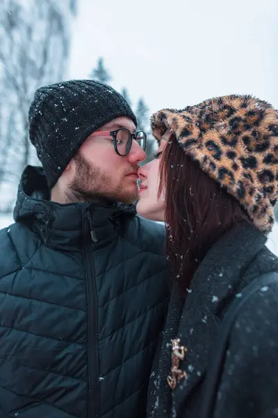 Güzel bir genç kız ve yakışıklı bir adam, şık kış kıyafetleri giymiş bir çift aşık parkta karla öpüşüyor. Aşk, arkadaşlık ve ilişkiler.
