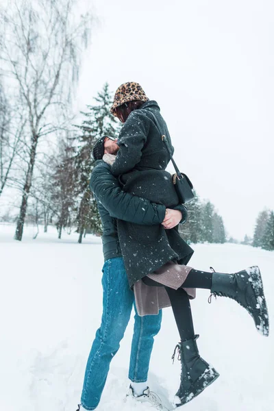 happy handsome man lifted his beautiful young girlfriend in a winter park with snow. Cheerful couple of lovers having fun and hugging