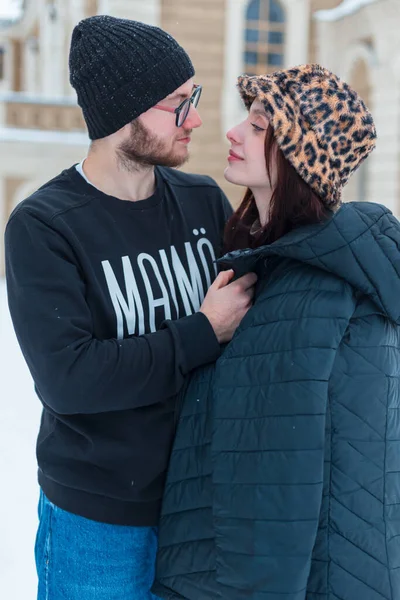 Moda kışı kıyafetleri içinde güzel, mutlu, genç aşıklar sokakta yan yana duruyorlar. Yakışıklı bir adam kız arkadaşını dışarıda sıcak tutmak için bir ceket verdi.