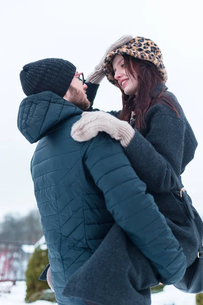Şapkalı, ceketli ve eldivenli şık kış kıyafetleri içinde sokaklarda eğlenen mutlu ve şık aşıklar. Havalı adam kaldırdı ve güzel kız arkadaşını kollarına aldı.