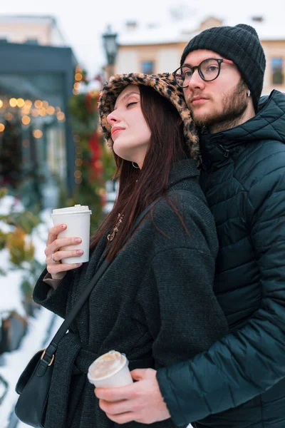 Şık, genç ve güzel aşıklar kışlık kıyafetlerini giymiş kahve içiyor, sarılıyor, dinleniyor ve kış günü karla birlikte şehirde yürüyor.