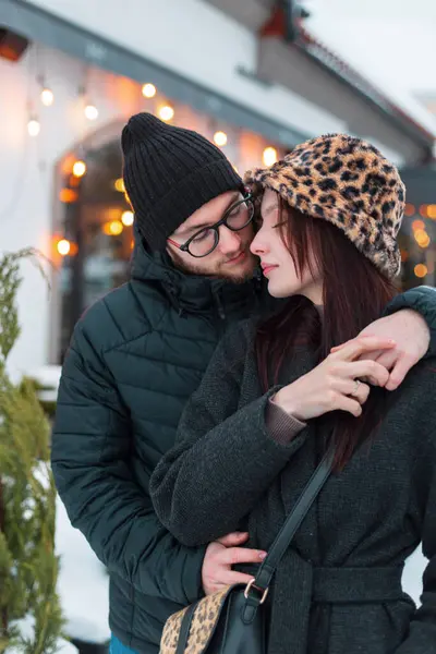 Güzel, genç moda aşıkları şehirde birlikte yürüyüp sarılıyorlar. Noel dekorunun arka planında şık kışlık giysiler içinde yakışıklı bir adam ve güzel bir kız.