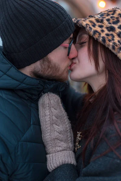 Şehirde öpüşen iki güzel sevgili, yakın plan. Güzel, genç bir kadın, şık kışlık elbiseli, ceketli ve eldivenli bir adamı öpüyor.
