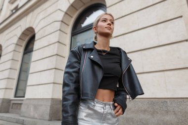 Havalı, siyah deri ceketli güzel bir kadın model. Şehirde klasik bir binanın yanında yürüyor..