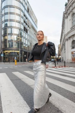 Deri ceketli ve etekli gündelik giysiler içinde güzel şehir moda kadını şehirde yaya caddesinde yürüyor.