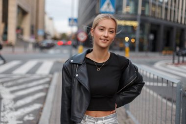 Moda rock kıyafetleri içinde, deri ceketli, şehirde yürüyen mutlu, güzel bir kadın manken.
