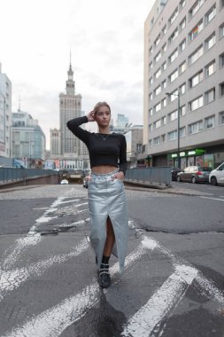 Moda elbisesi içinde, siyah bluzlu ve gümüş etekli güzel, genç ve şık bir kız şehirde yol boyunca yürüyor..