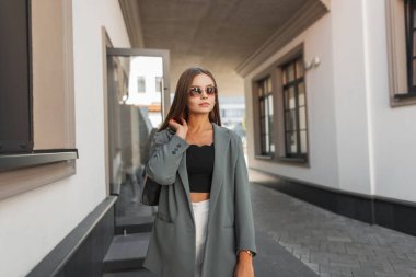 Şehirde güzel, başarılı, güneş gözlüklü, moda elbiseli, spor ceketli ve çantalı bir iş kadını.