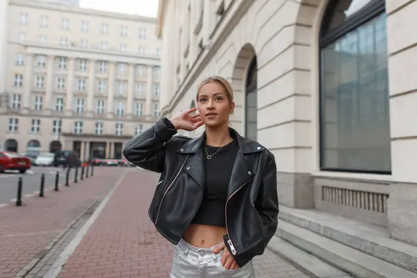 Şık, genç ve güzel bir bayan model, şehirde deri ceketli geziyor.