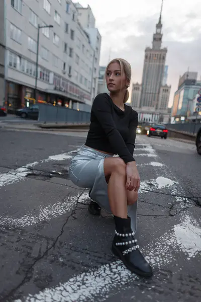 Moda kıyafetleri içinde güzel bir kız, etek ve üstüyle şehirde oturur ve poz verir.