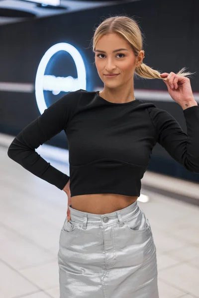 Fashionable beautiful girl model in fashion clothes with a black top and silver skirt posing at a subway station
