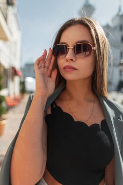 Güneşli bir günde, şık güneş gözlüklü, modaya uygun kıyafetler giyen ve spor ceketli zarif bir genç kız mankeni. Şık kadın gözlük takıyor.