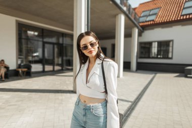 Havalı, mutlu, modaya uygun, gülümseyen, klasik güneş gözlüklü, şık bir çantayla şehirde dolaşan güzel bir manken kız.