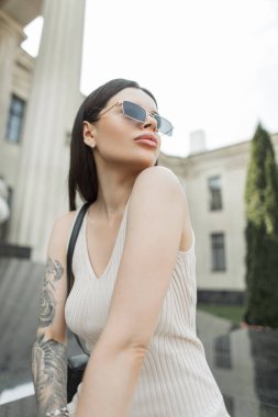 Modaya uygun bej elbiseli, eski güneş gözlüklü, yeni yüzlü güzel bir kadın model şehirde oturuyor. Güzel bayan.