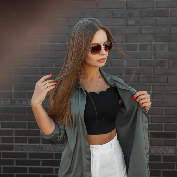 Siyah tuğladan bir duvarın yanında duran, üzerinde moda gömleği olan, klasik güneş gözlüklü, sokak güzeli, zarif model kız.
