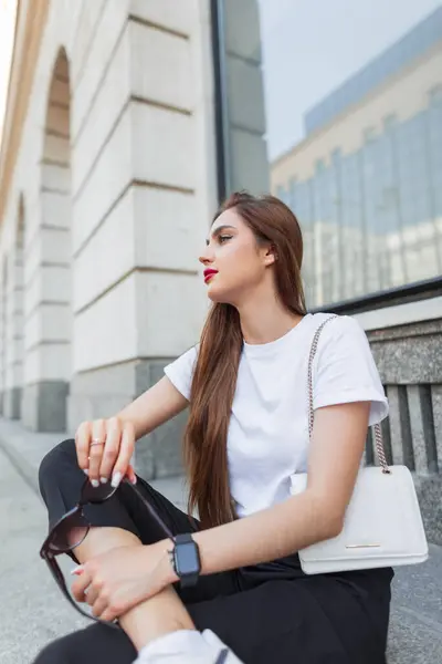 スタイリッシュな白いTシャツのファッショナブルな美女は 市内のヴィンテージビル近くのステップに座っています かわいい都市女性 — ストック写真