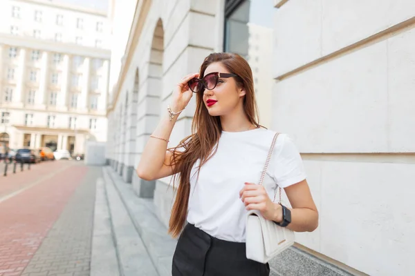 スタイリッシュな美しい都市の新鮮な女性モデル ファッショナブルなホワイトモックアップTシャツで街を歩き トレンディなサングラスを置きます — ストック写真