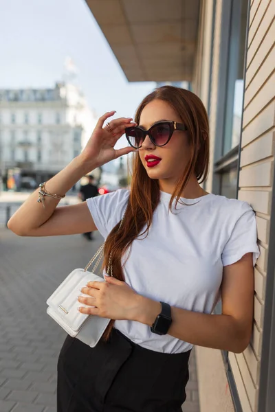街のファッショナブルなサングラスに白いバッグが置かれたファッション服でスタイリッシュな美しい若い女性 — ストック写真