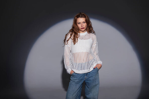 Модные красивые стильные девушки-модели в модной одежде с белым модным свитером и винтажными джинсами стоят в студии на темном фоне
