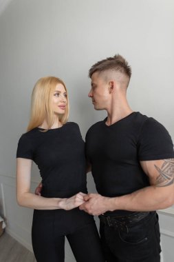 Bakır renkli siyah elbiseli güzel, genç, modaya uygun bir çift beyaz arka planda tişört tasarlıyor. Güzel sarışın kız ve yakışıklı adam.