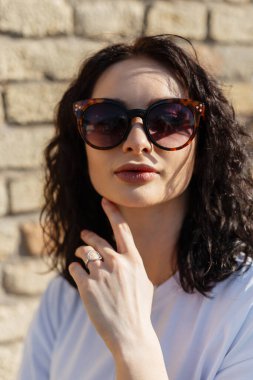 Havalı güneş gözlüklü beyaz tişörtlü, kıvırcık saçlı, şık bir kadın mankeni.