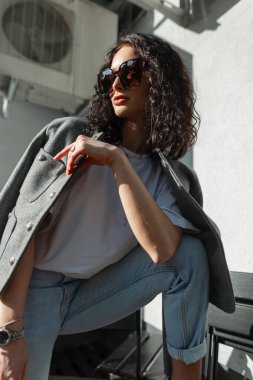 Güneş gözlüklü, şık, beyaz tişörtlü ve kot pantolonlu güzel, çekici bir manken.