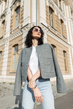 Güneş gözlüklü, şık, beyaz tişörtlü ve kot pantolonlu, şık, genç ve güzel kıvırcık kadın mankeni.