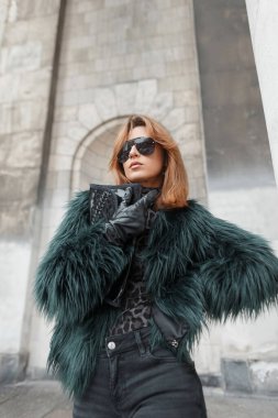 Moda kıyafetleri içinde, eldivenli ve çantalı şık bir kadın mankeni klasik binanın yanında poz veriyor.